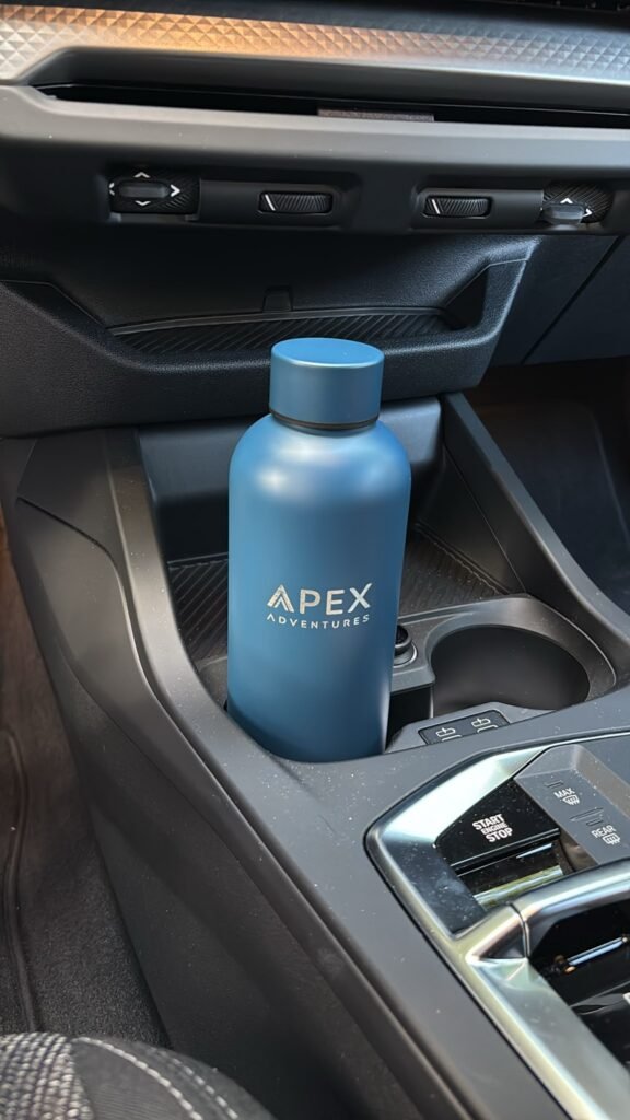 Blaue Trinkflasche mit graviertem Firmenlogo APEX Adventures im Getränkehalter eines Autos